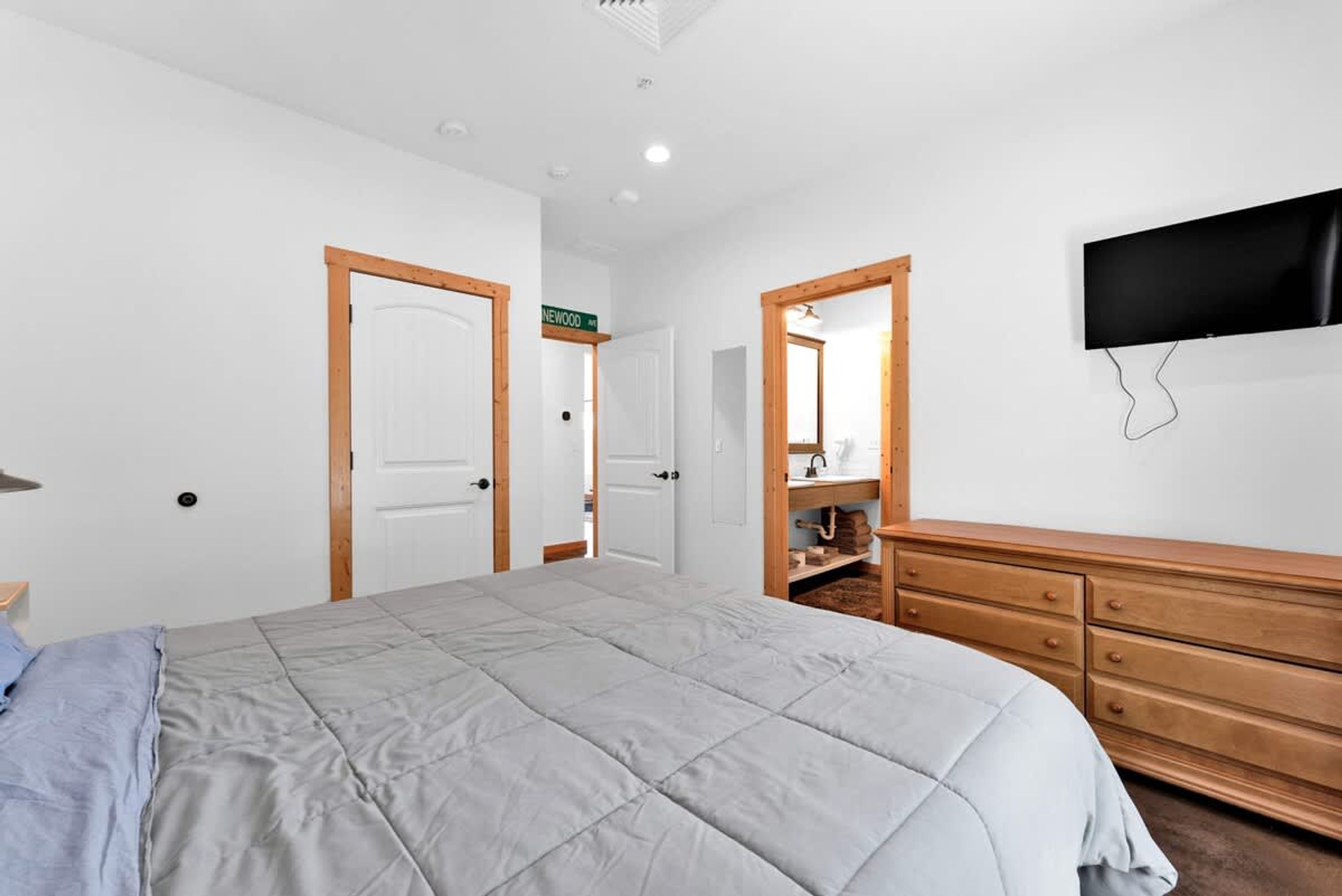 Une chambre avec un grand lit, une armoire en bois et un téléviseur fixé au mur.