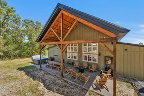 A covered outdoor patio with wooden furniture, a hot tub, and a grill area. - 8-bedroom Branson Retreat- Hot Tub Porch Swings (Branson)