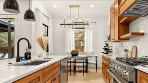 A modern kitchen with wooden cabinets, a stainless steel stove, and pendant lighting. - Austin Family Retreat at Ember House (Austin)