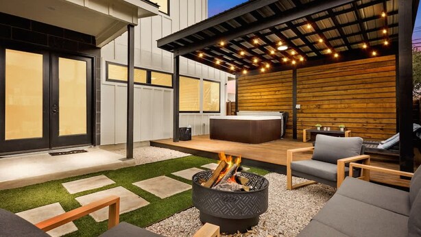 A modern outdoor patio with a fire pit, seating, and a covered area with string lights. - Austin Family Retreat at Ember House (Austin)
