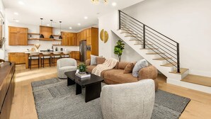 A modern living room with a sofa, coffee table, and a staircase leading to an upper level. - Austin Family Retreat at Ember House (Austin)