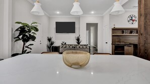 Een moderne eetruimte met een grote witte marmeren tafel, drie hanglampen, een televisie en een decoratie met Texaanse thema's.