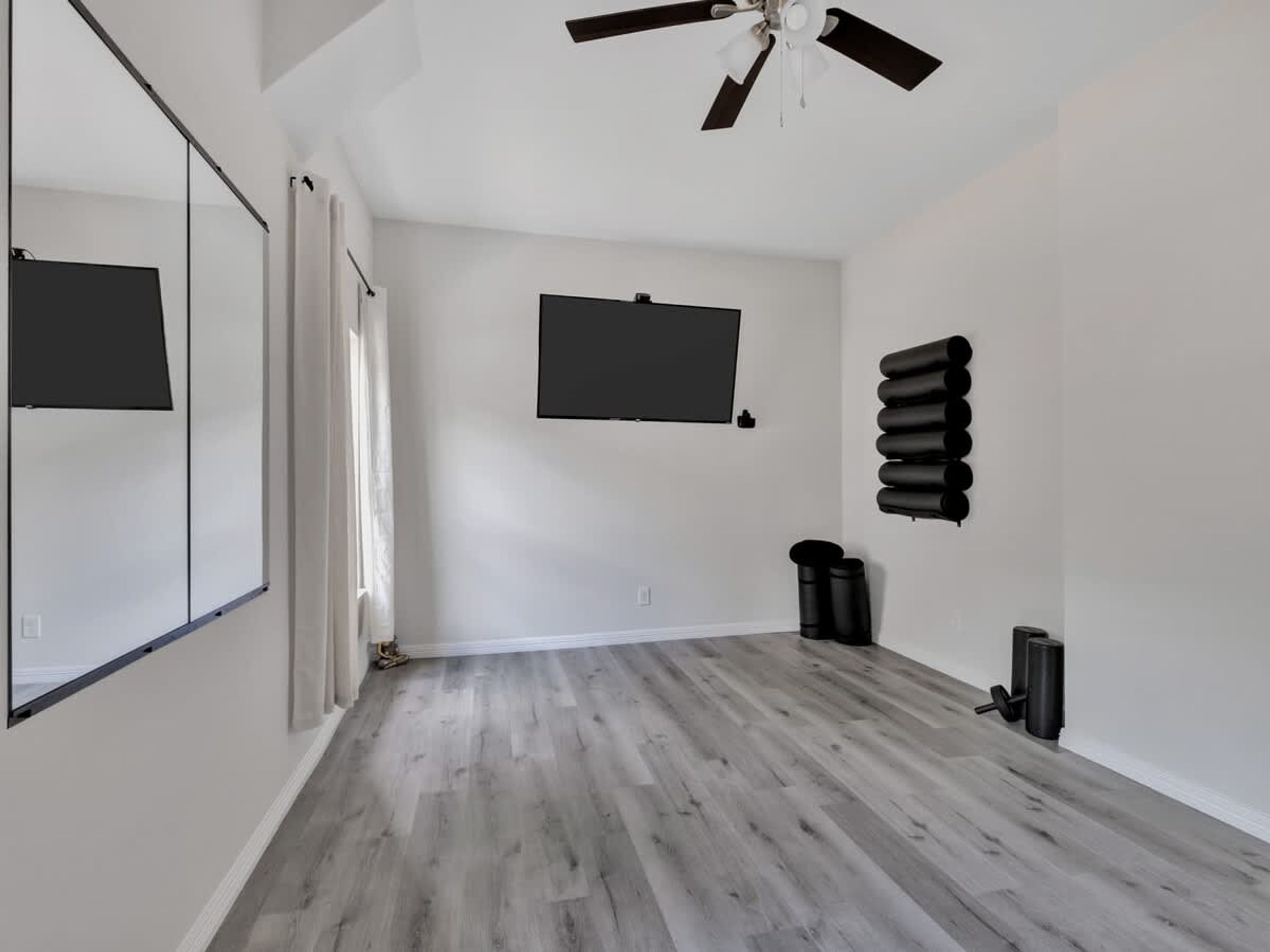 Ein Zimmer mit Deckenventilator, einem angebrachten Fernseher und mehreren schwarzen, zylindrischen Objekten an der Wand.