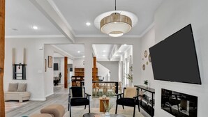 Een ruime woonkamer met een modern design, voorzien van een grote flatscreen televisie aan de muur, een comfortabele zithoek met banken en stoelen, en een houten salontafel.