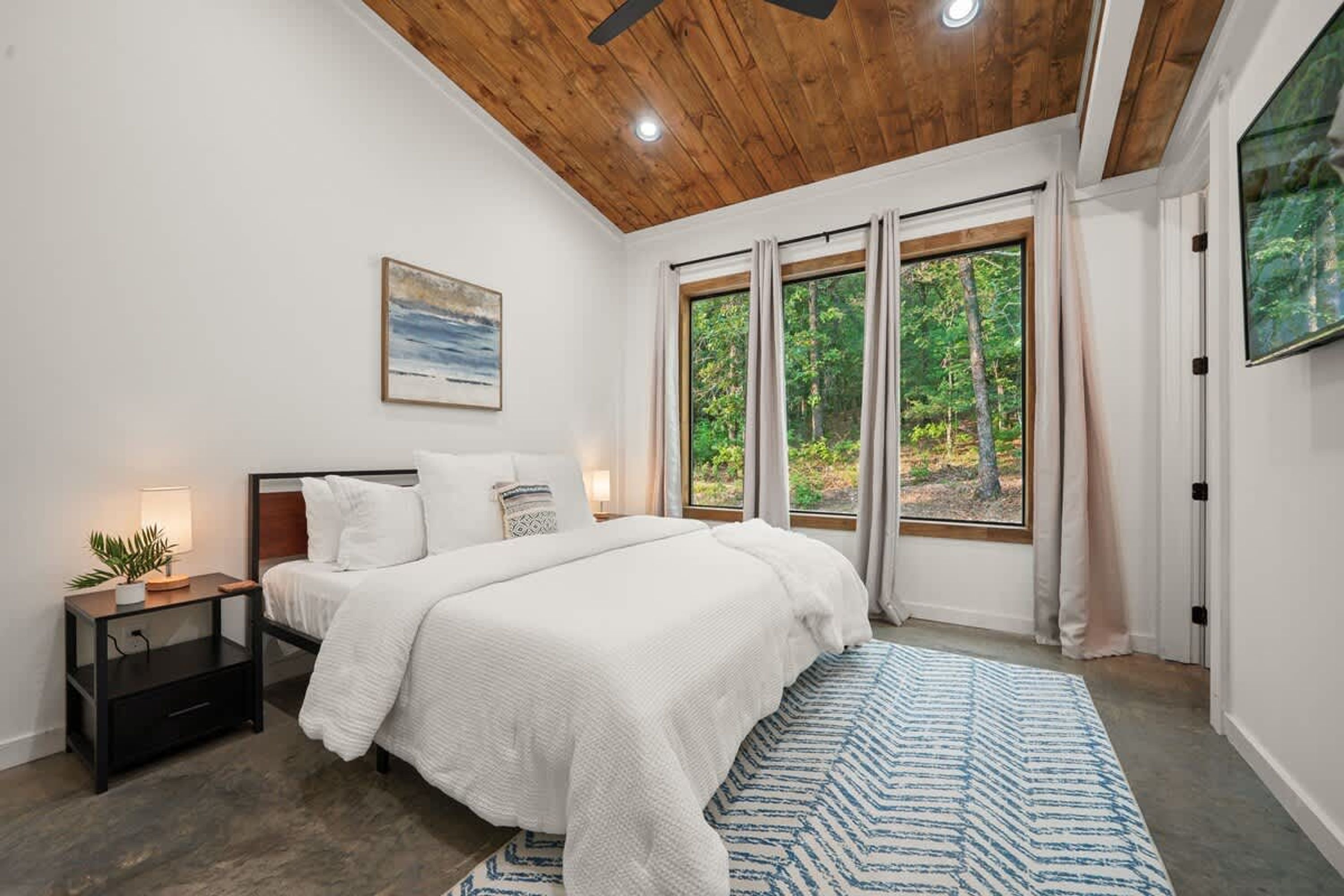 A bedroom with a large bed, a nightstand, a window with curtains, and a painting on the wall.