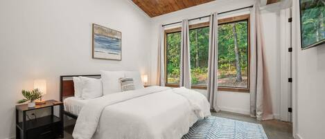A bedroom with a large bed, a nightstand, a window with curtains, and a painting on the wall.