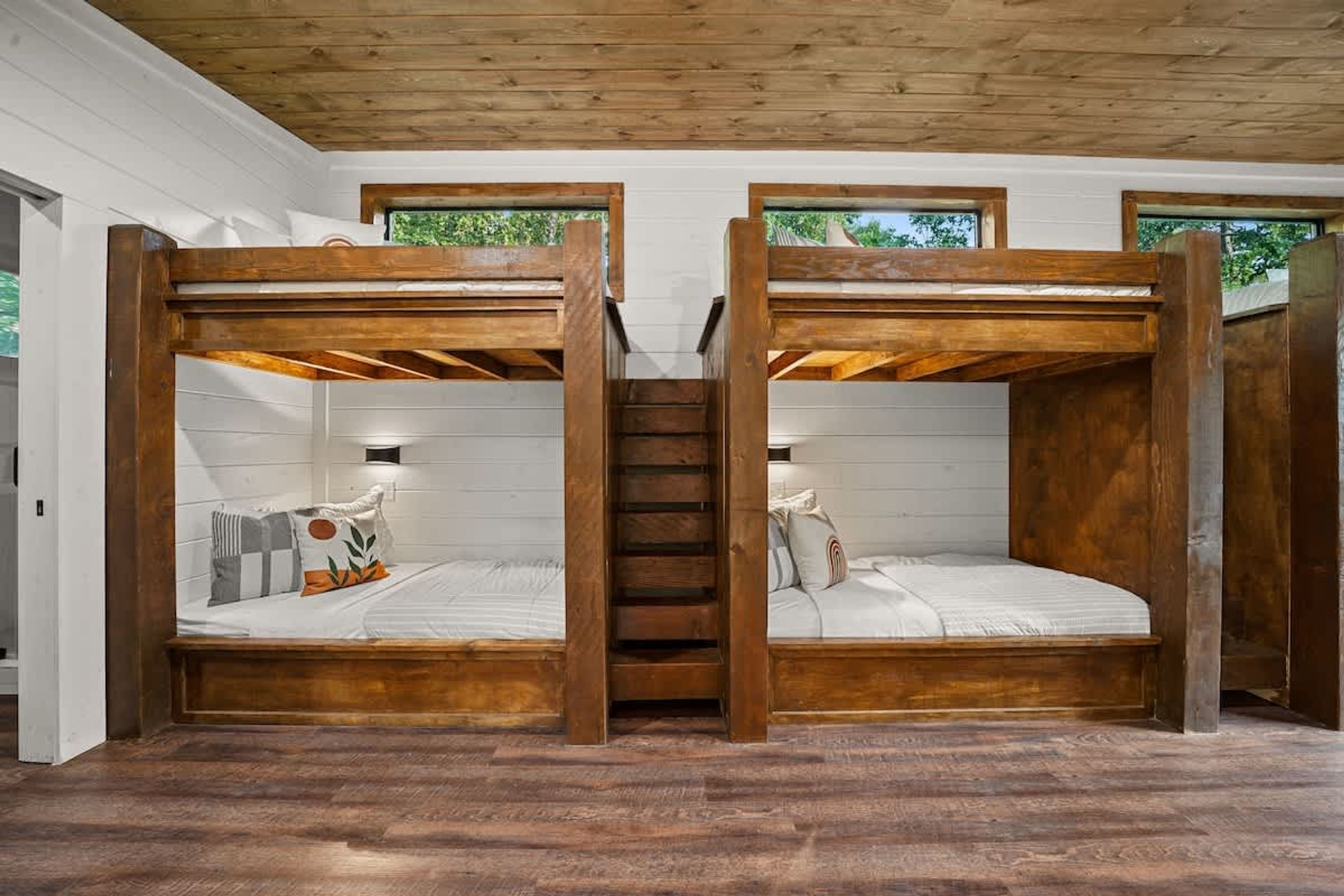 Dormitorio con literas, una escalera de madera y paredes blancas.