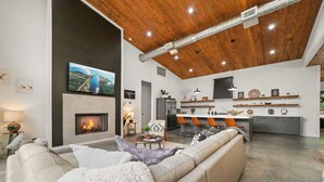 A modern living room with a fireplace, a large TV, and a dining area with orange chairs. - Hgtv Cabin- 2 Private Acres -patio Oasis Dogs OK (Broken Bow)