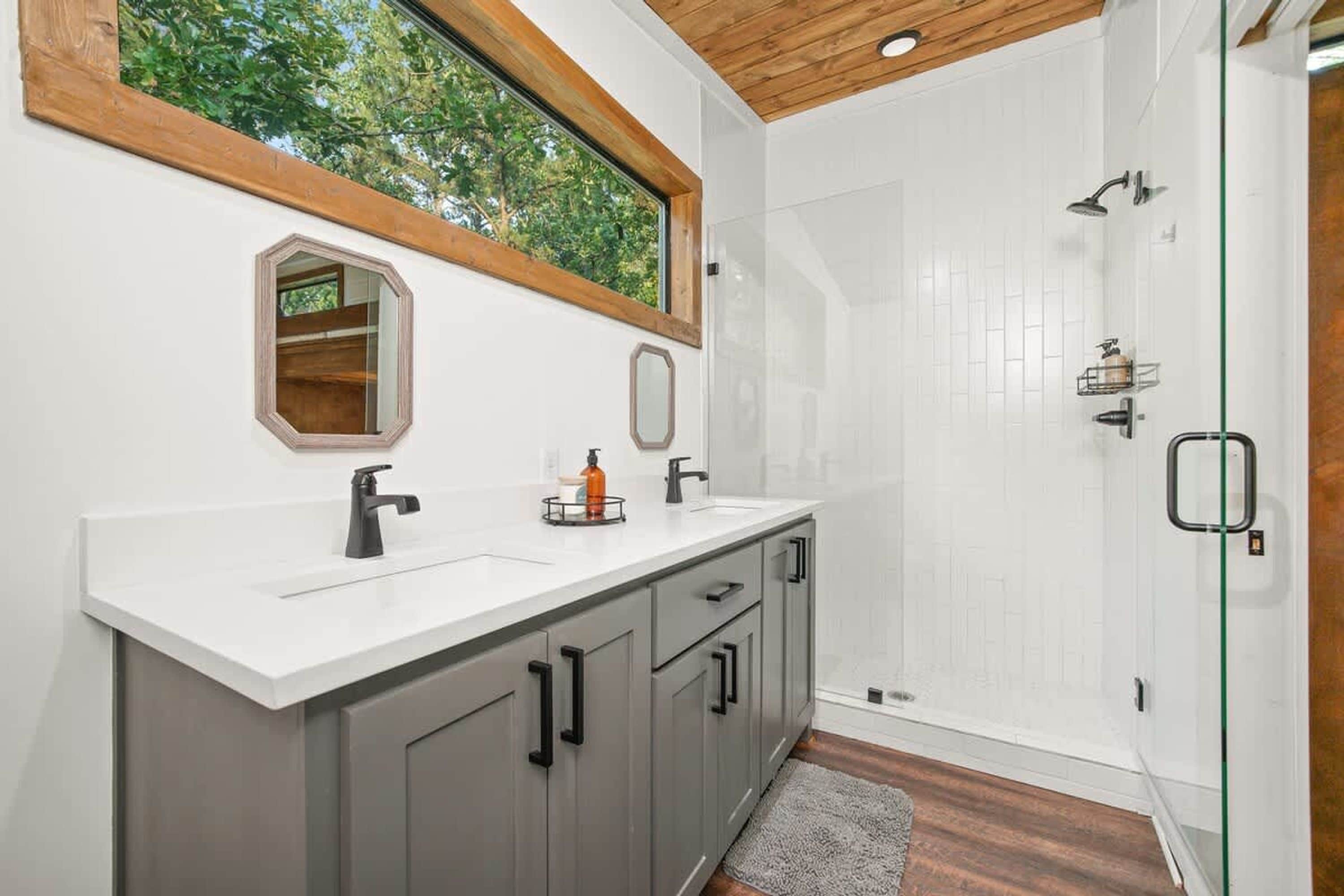 Een moderne badkamer met een groot raam, een douche en een wastafel met spiegel.