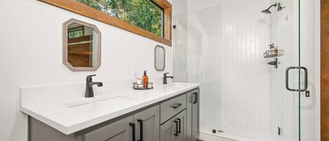 A modern bathroom with a large window, a shower, and a vanity with a mirror.