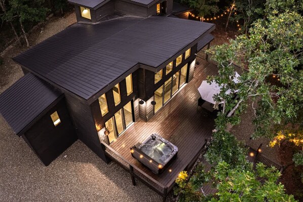 Una casa moderna con jacuzzi en la terraza, rodeada de árboles y luces colgantes.