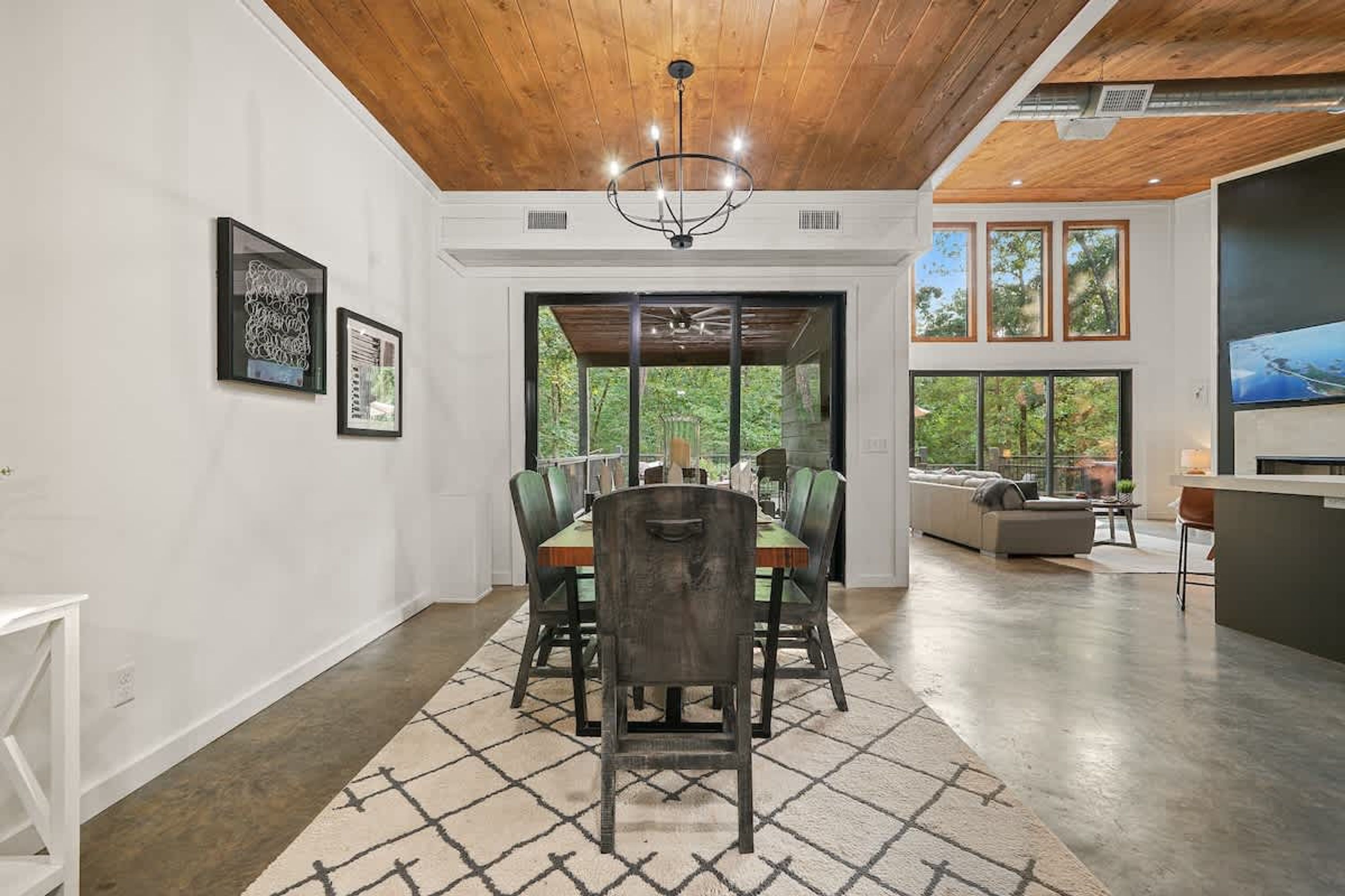 A spacious dining area with a wooden ceiling, a chandelier, and a large window offering a view of the outdoors.