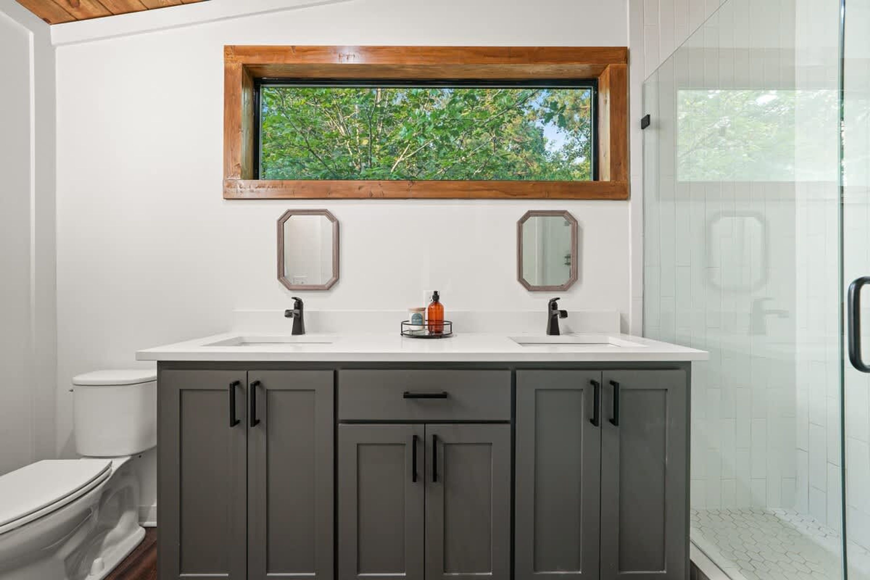 Un baño con ventana, dos lavamanos y una ducha.