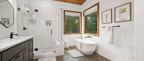Une salle de bain moderne équipée d’une douche, de toilettes et d’une baignoire. Elle se distingue par son plafond en bois, ses carreaux blancs et une grande fenêtre qui laisse entrer la lumière naturelle.
