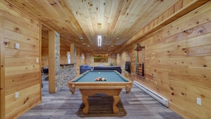Una habitación con paneles de madera, una mesa de billar, una pared de piedra y una chimenea.