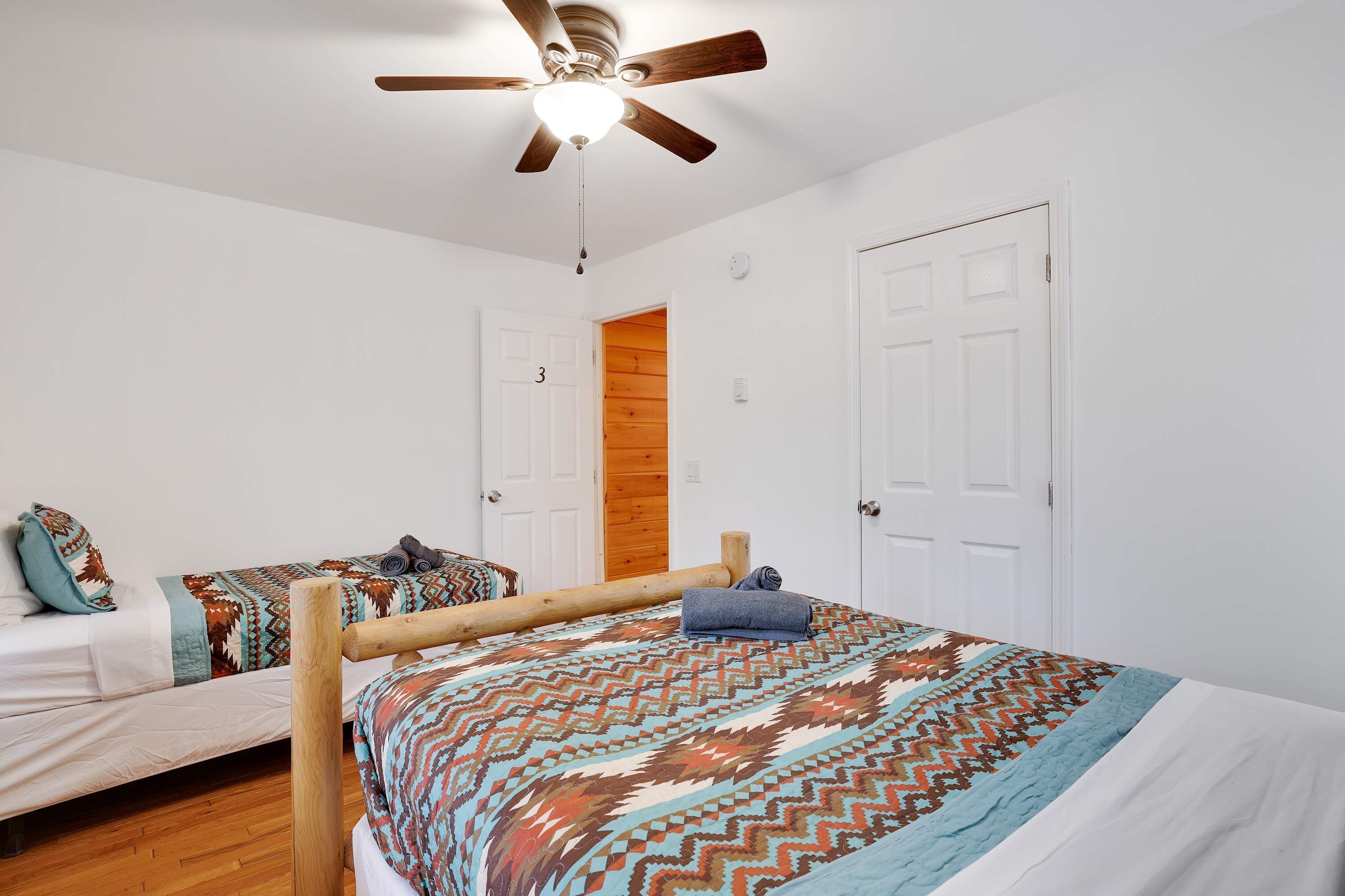 A bedroom with two beds, a wooden headboard, a ceiling fan, and white walls.