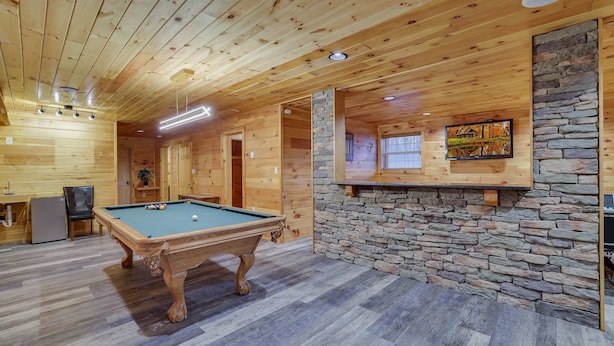 Un interior de madera con mesa de billar, pared de piedra e iluminación empotrada.