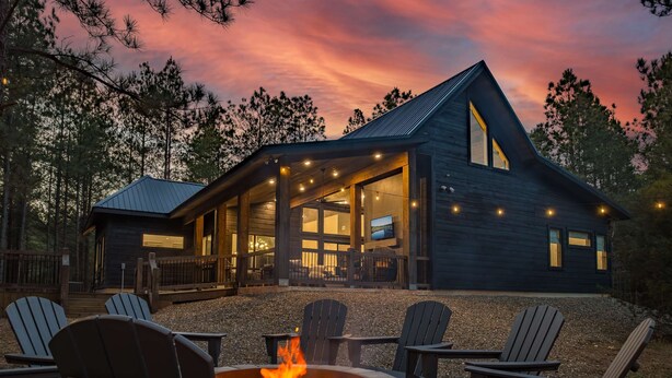 Een chalet met een vuurkuil en buitenmeubels, omgeven door bomen.
