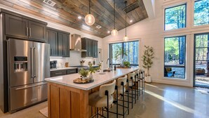 Een moderne keuken met een centraal eiland, roestvrijstalen apparatuur en een houten plafond.