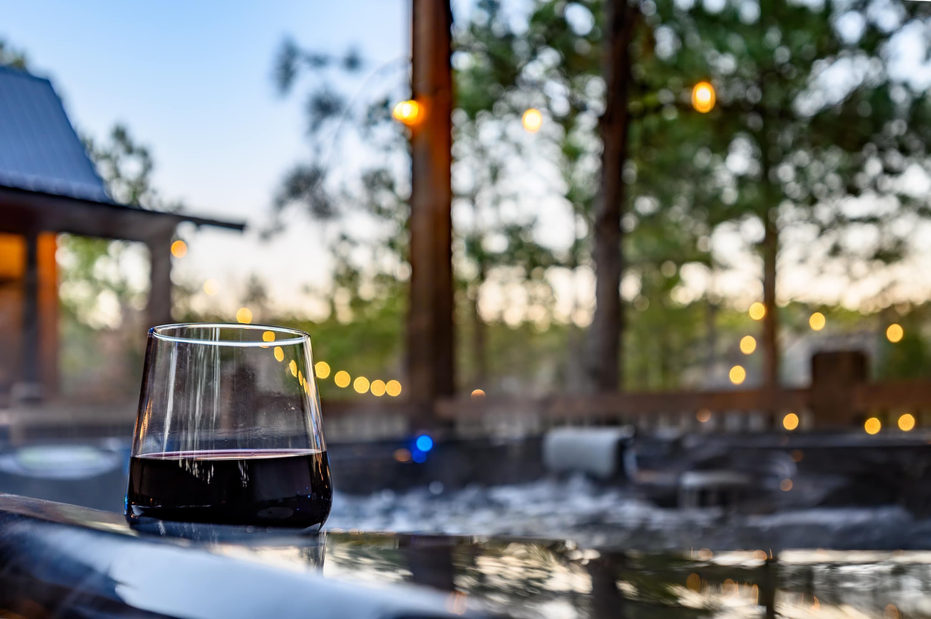 Un verre de vin rouge sur une table, avec une vue sur une piscine et des arbres en arrière-plan.