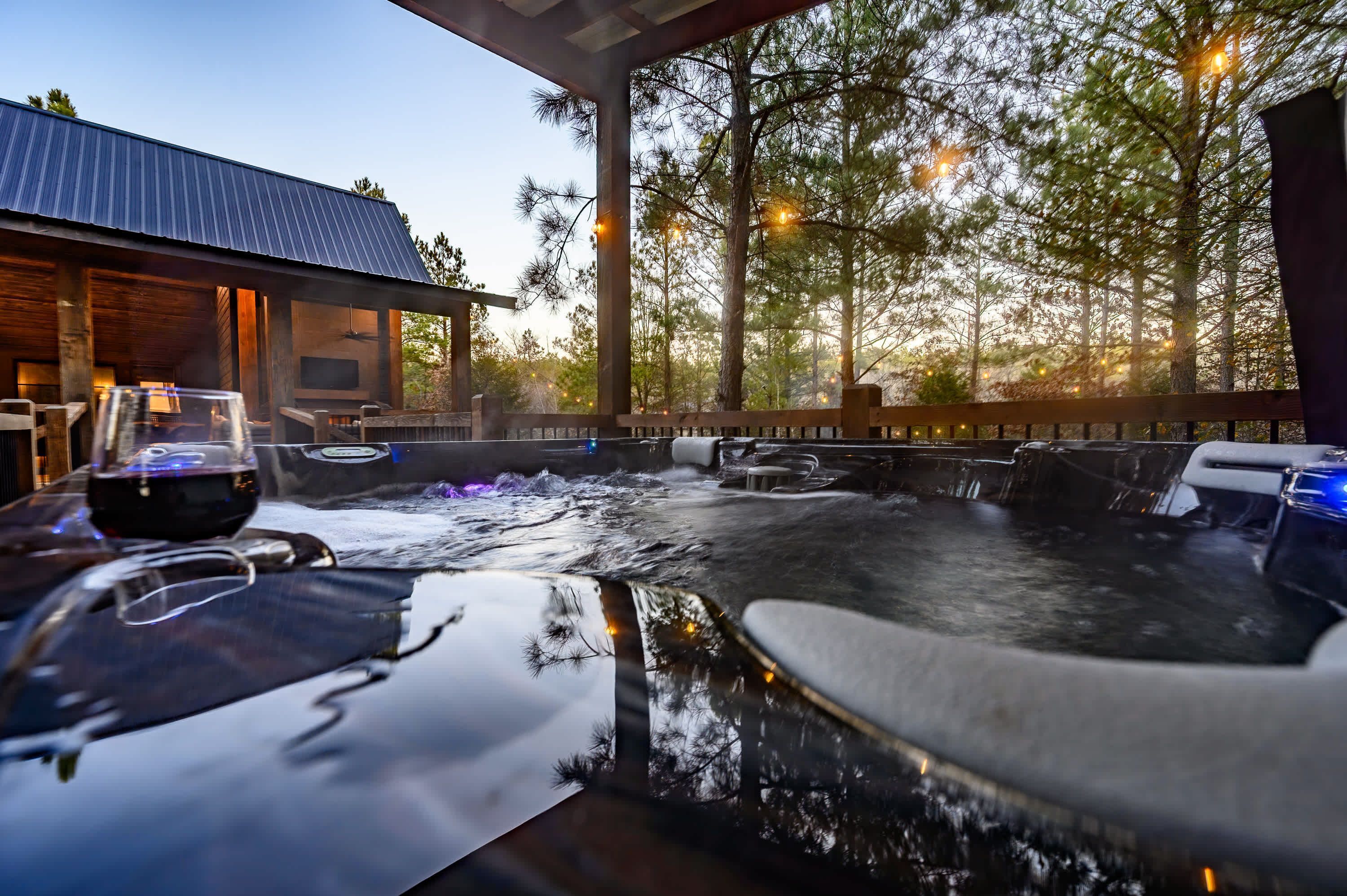 A hot tub area with a wooden deck, seating, and a view of trees.