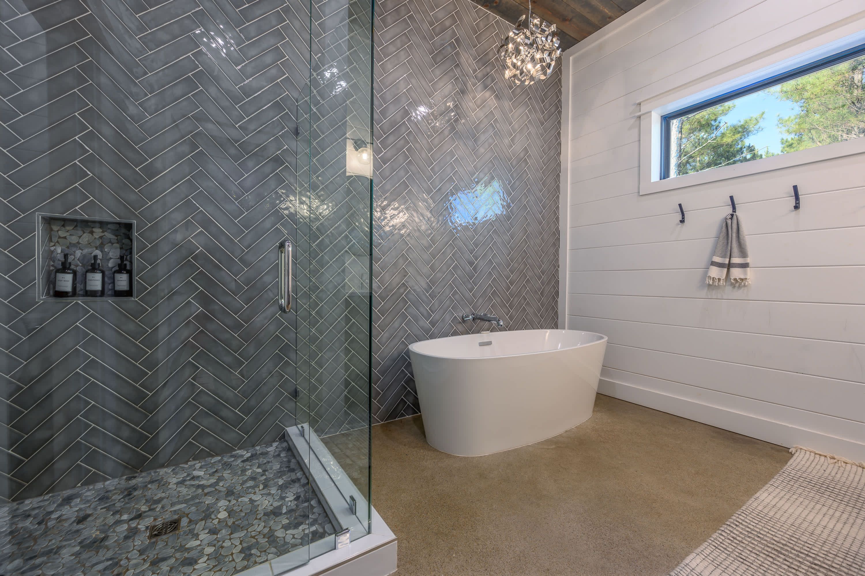Une salle de bain moderne avec un mur recouvert de carreaux disposés en motif chevron, une baignoire sur pieds et une cabine de douche en verre.