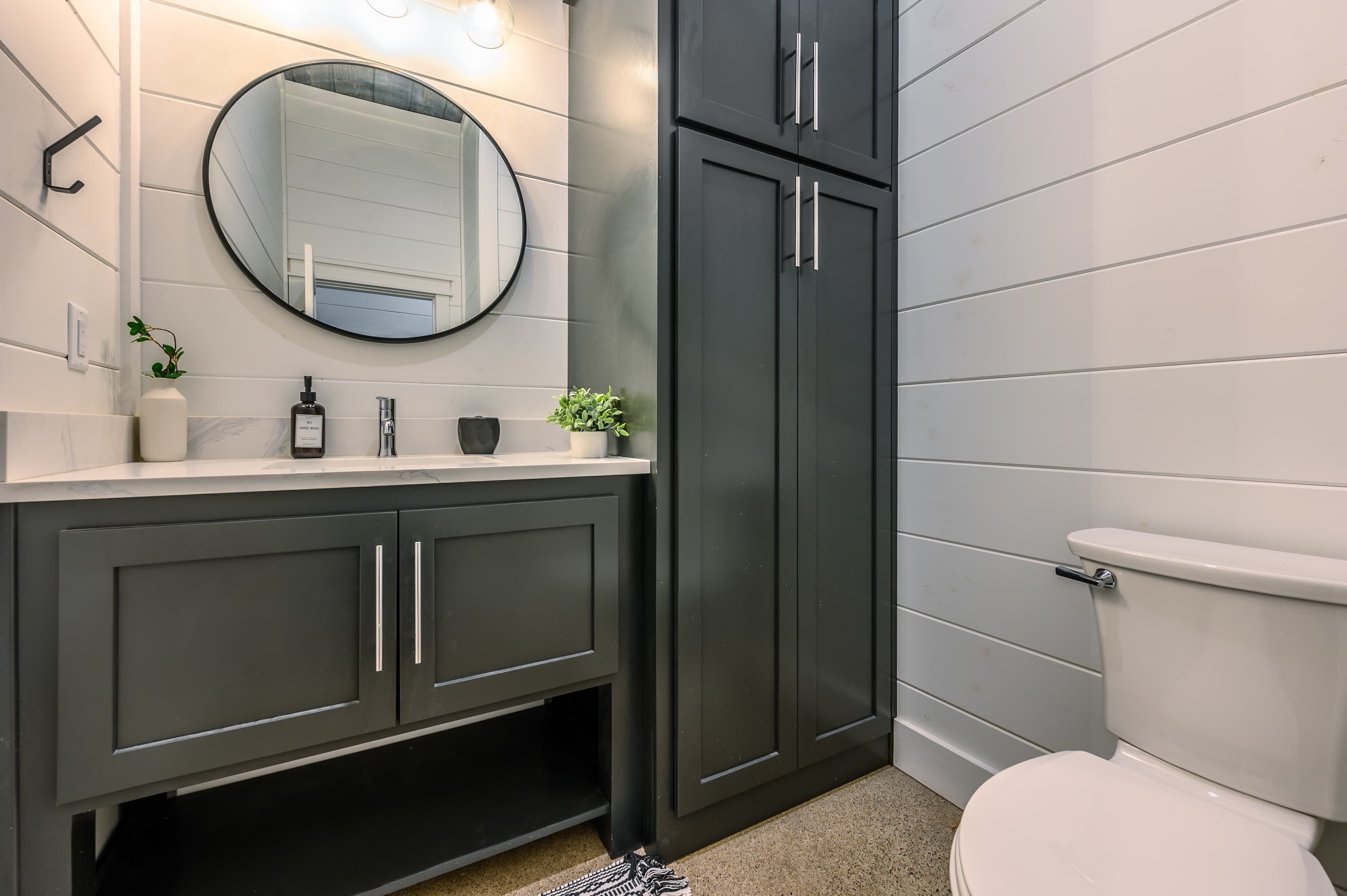 Een moderne badkamer met donkere kastjes, een ronde spiegel en een wit toilet.
