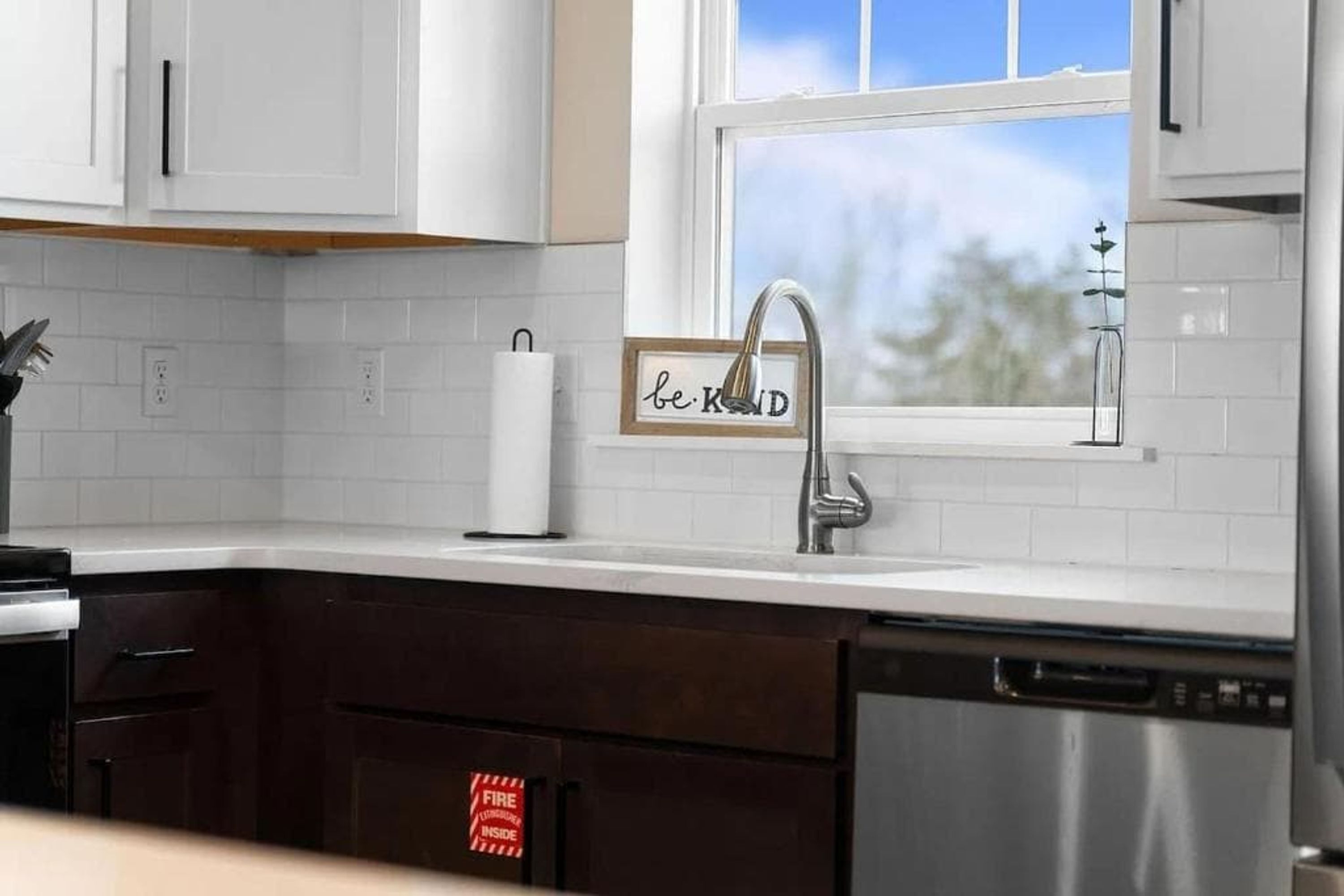 Een moderne keuken met witte kasten, een RVS vaatwasser en een raam met uitzicht op bomen.