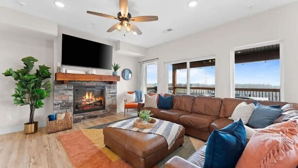 A spacious living room with a fireplace, leather sofas, a flat-screen TV, and large windows offering a view. - Modern Getaway w Hot Tub Arcade Stunning Views (Branson)