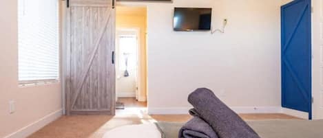 A bedroom with a bed, a TV mounted on the wall, a sliding door, and a view into another room.