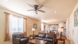 A living room with a sofa, two armchairs, a coffee table, and a ceiling fan. There is a kitchen in the background. - Elegant Spacious 4BR Home Peyton (Elbert)