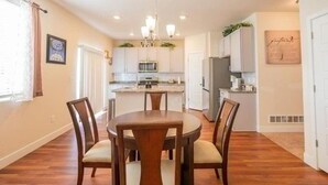 A dining area with a round wooden table and four chairs, a kitchen in the background, and a framed artwork on the wall. - Elegant Spacious 4BR Home Peyton (Elbert)