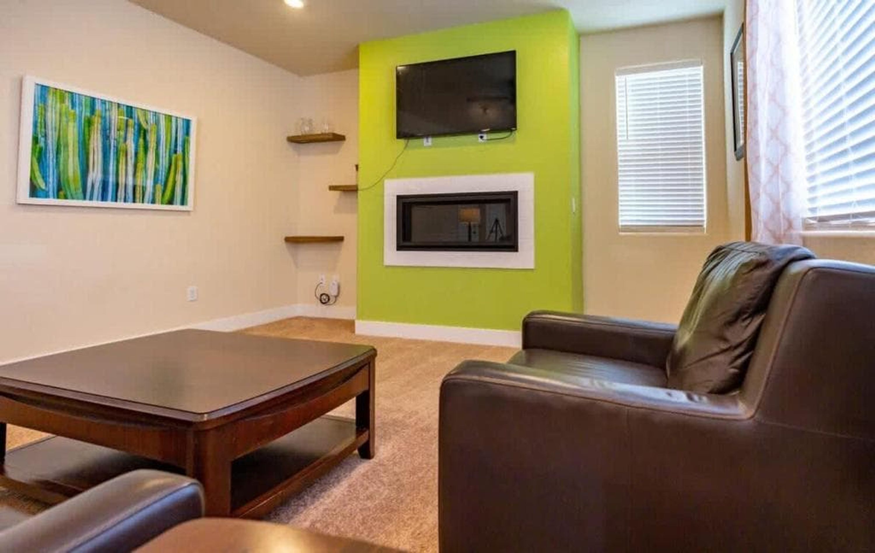 Een woonkamer met een bruine leren bank, een houten salontafel, een aan een groene muur bevestigde televisie en een open haard.