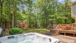 Un bain à remous dans un jardin arboré, avec une terrasse et des escaliers menant à une maison.