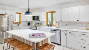 Une cuisine moderne avec des meubles blancs, des appareils en acier inoxydable, un îlot central doté de tabourets et un luminaire suspendu.