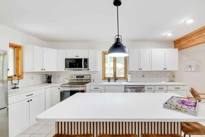 A modern kitchen with white cabinetry, a central island, and a black pendant light. - A Family Woodland Retreat (Albrightsville)