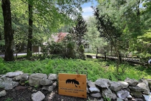 Schild für Woodlands Hideaway von Loma Homes, umgeben von einer Steinmauer und üppigem Grün.
