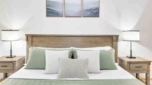 Un lit bien fait, avec une tête de lit en bois, deux tables de chevet avec des lampes et trois tableaux encadrés accrochés au mur.