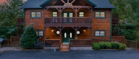 A two-story log cabin with a balcony, a front porch, and a driveway.