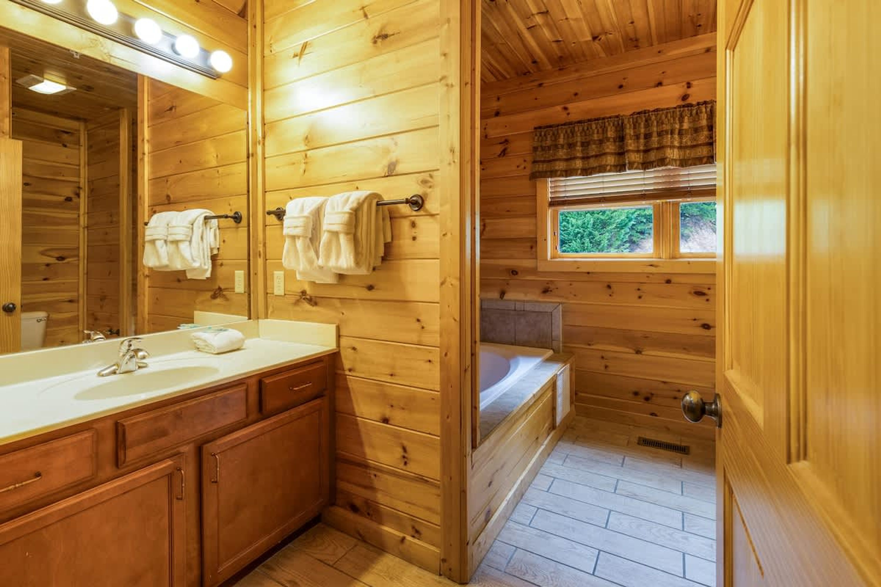 A wooden cabin bathroom with a sink, mirror, towels, and a bathtub.