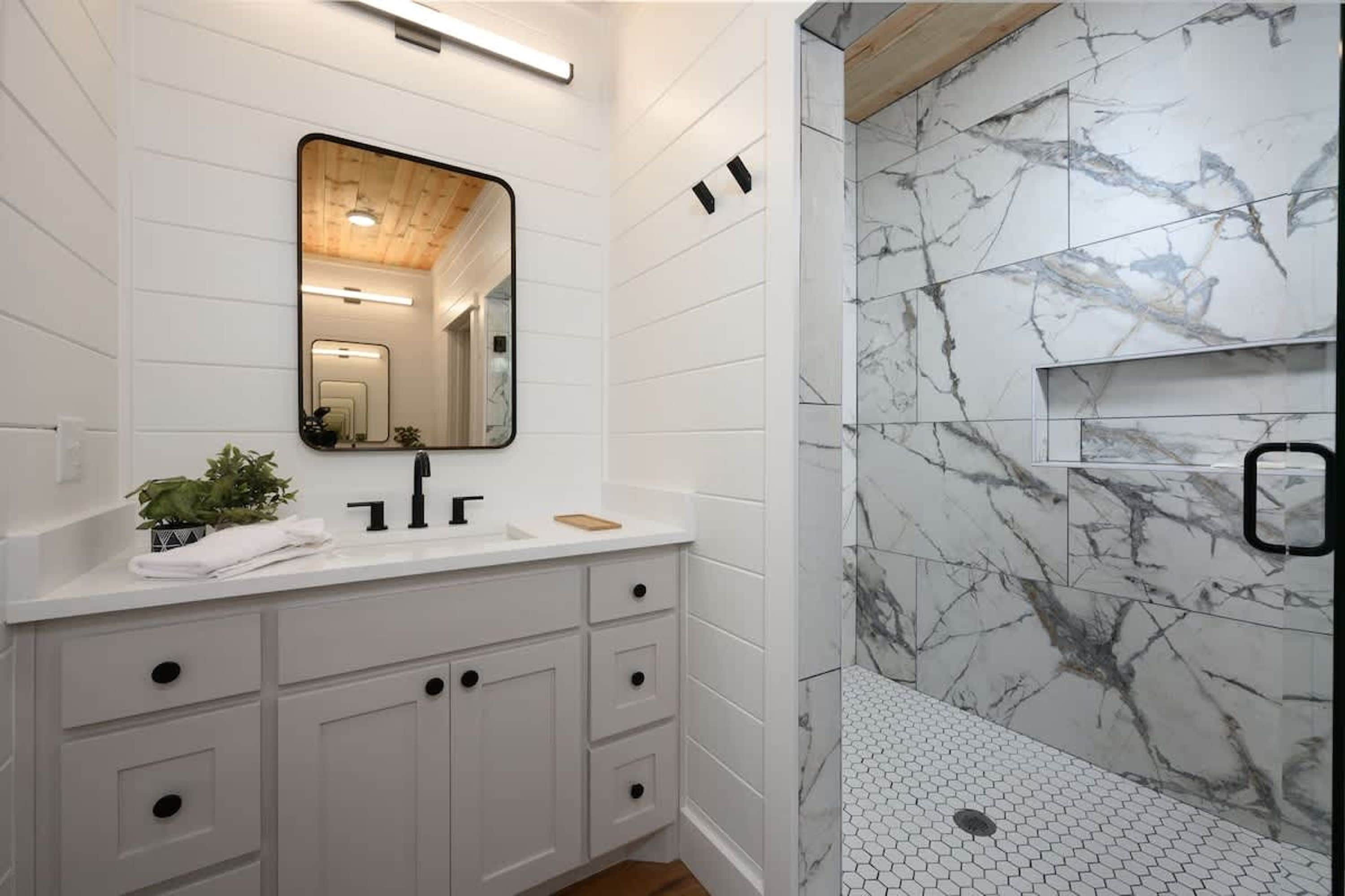 A modern bathroom with a white vanity, a mirror, and a shower with marble walls.