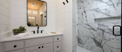 A modern bathroom with a white vanity, a mirror, and a shower with marble walls.