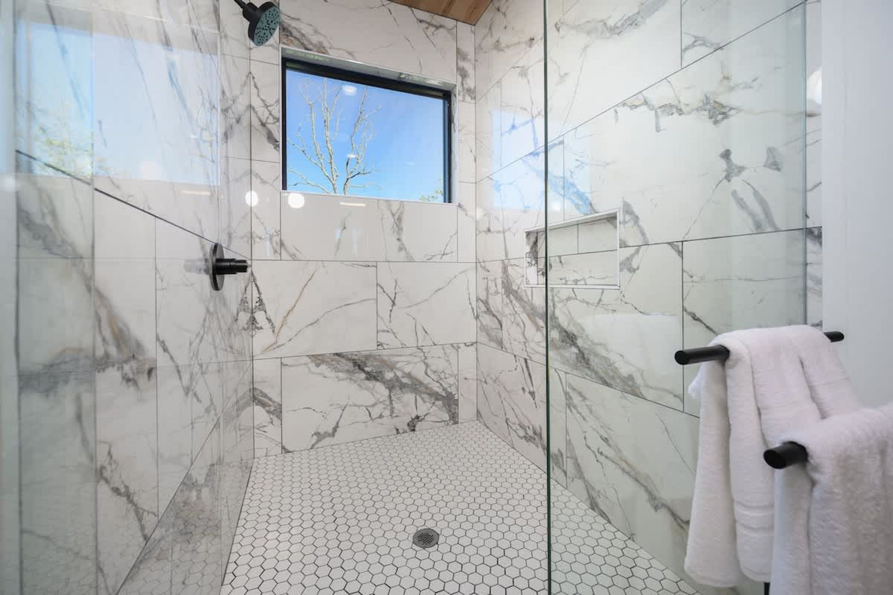 A modern bathroom with marble walls, a glass shower enclosure, and a visible window.