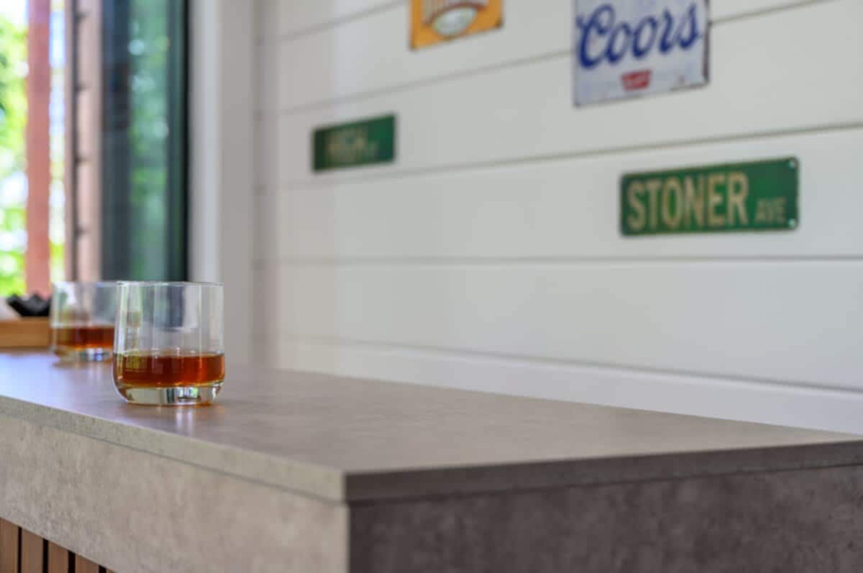 Baaritiskialue, jossa on lasit täynnä kullanruskeaa juomaa, Coors-mainos ja Stoner Avenue -kyltti seinällä.