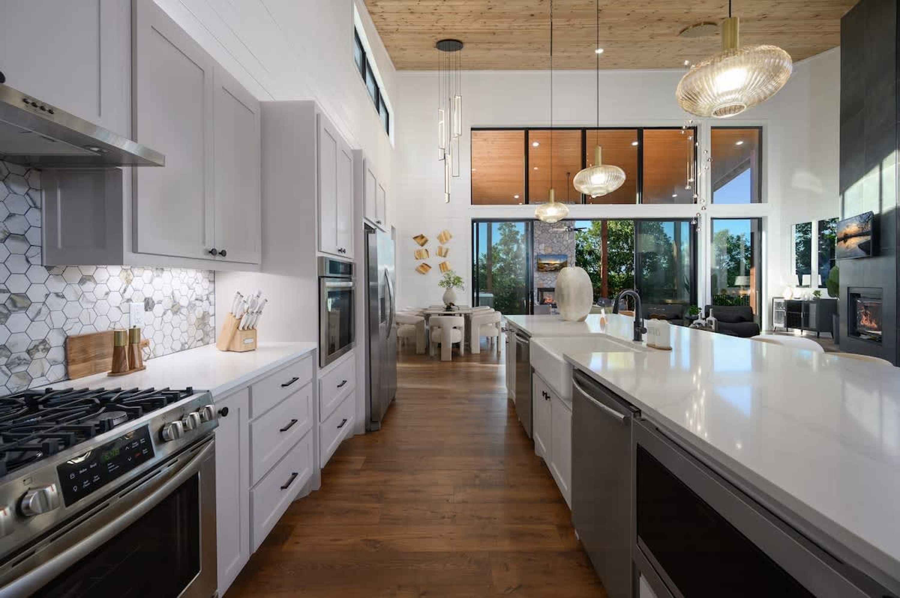 Une cuisine moderne avec des meubles blancs, un grand îlot central, des appareils électroménagers en acier inoxydable et un plafond en bois.