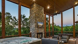 A hot tub, stone fireplace, and outdoor seating on a wooden deck with a view of trees. - Sit n Go Family Retreat Poker Darts Billiards (Broken Bow)