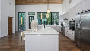A modern kitchen with a large island, stainless steel appliances, and a view of the outdoors. - Sit n Go Family Retreat Poker Darts Billiards (Broken Bow)