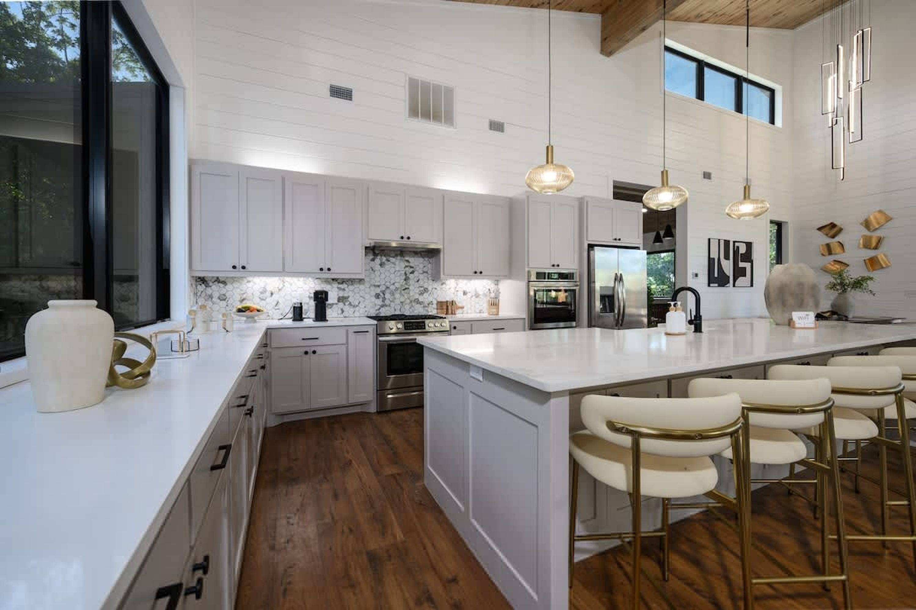 A modern kitchen with white cabinetry, a large island with bar stools, stainless steel appliances, and pendant lighting.