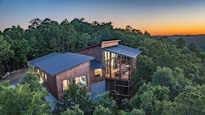 A modern house with a large deck, surrounded by dense forest. - Sit n Go Family Retreat Poker Darts Billiards (Broken Bow)