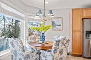 Un comedor con una mesa redonda, sillas estampadas con motivos florales, un jarrón azul con follaje y una araña.